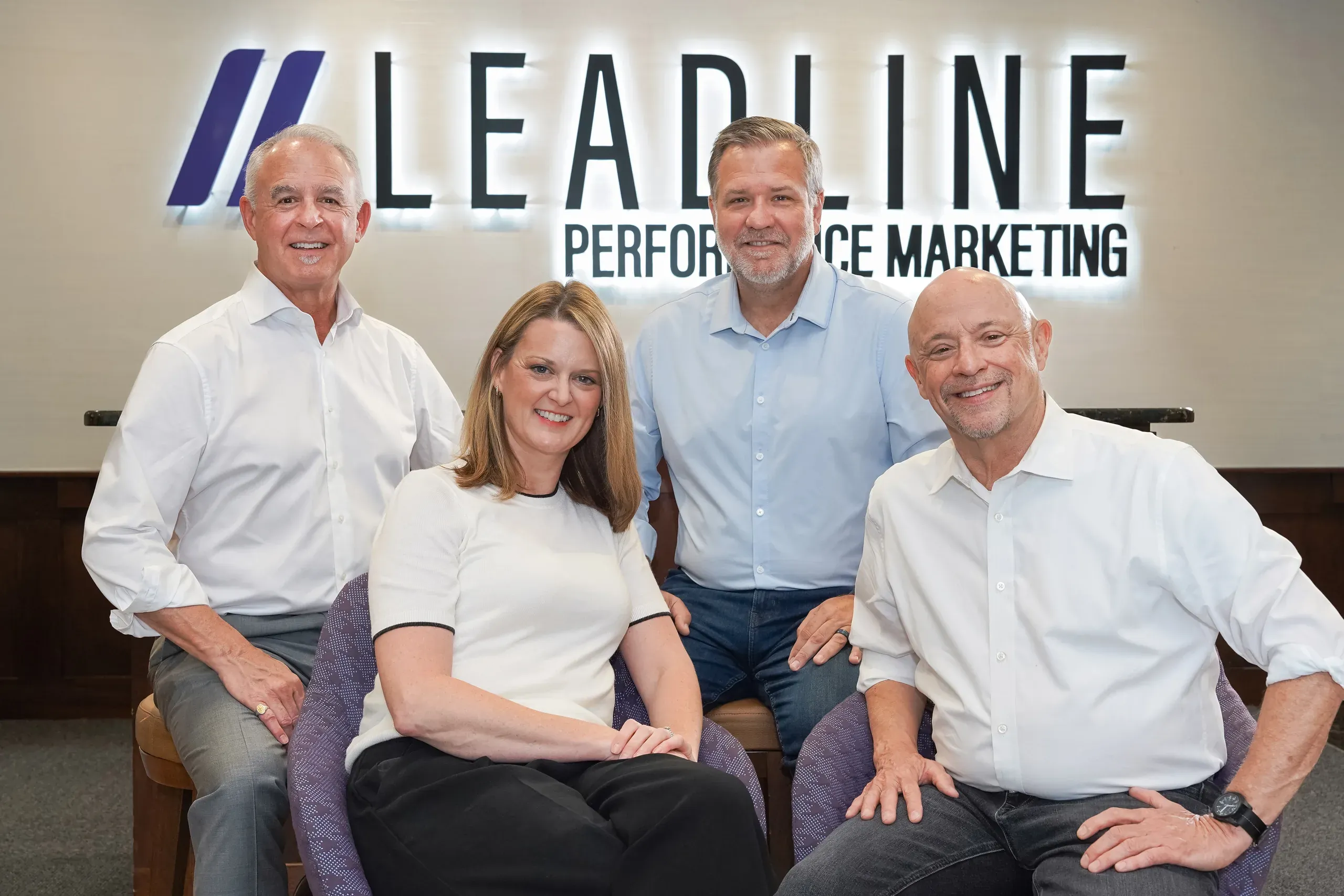 Four partners of Leadline Performance Marketing pose together in front of the company logo, smiling and dressed in business-casual attire.