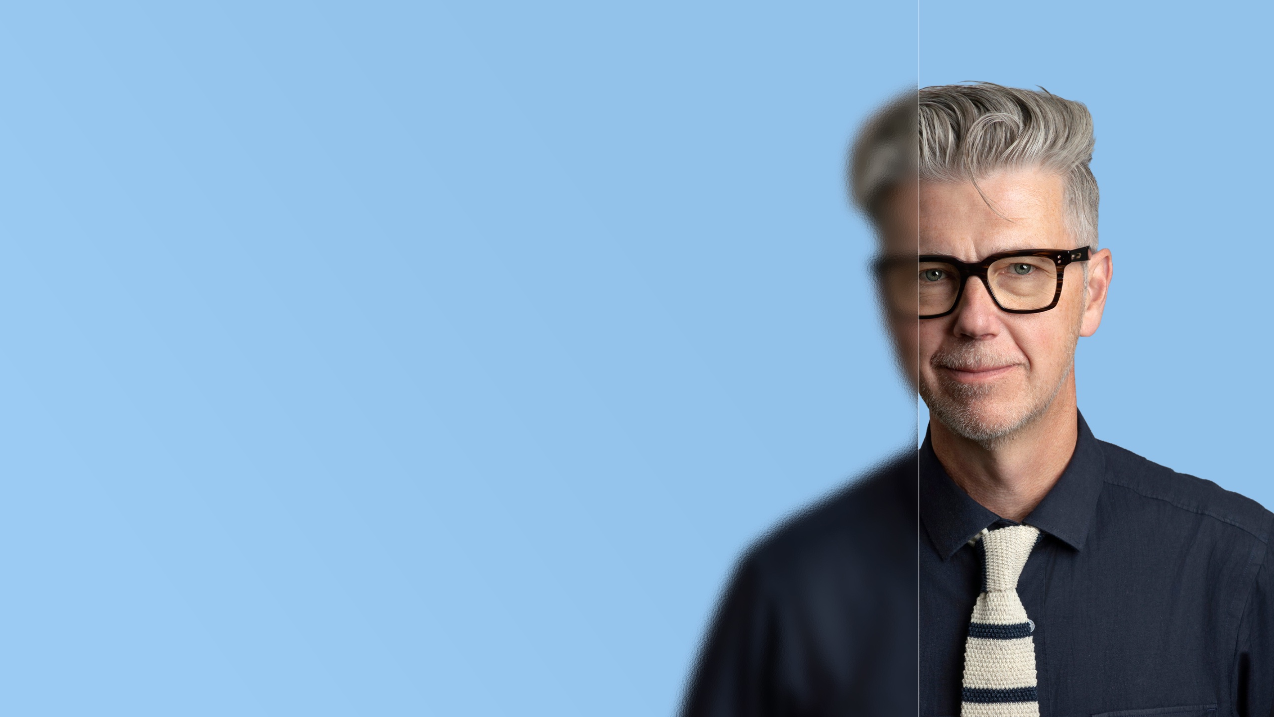 Smiling professional with glasses in a navy shirt and knit tie