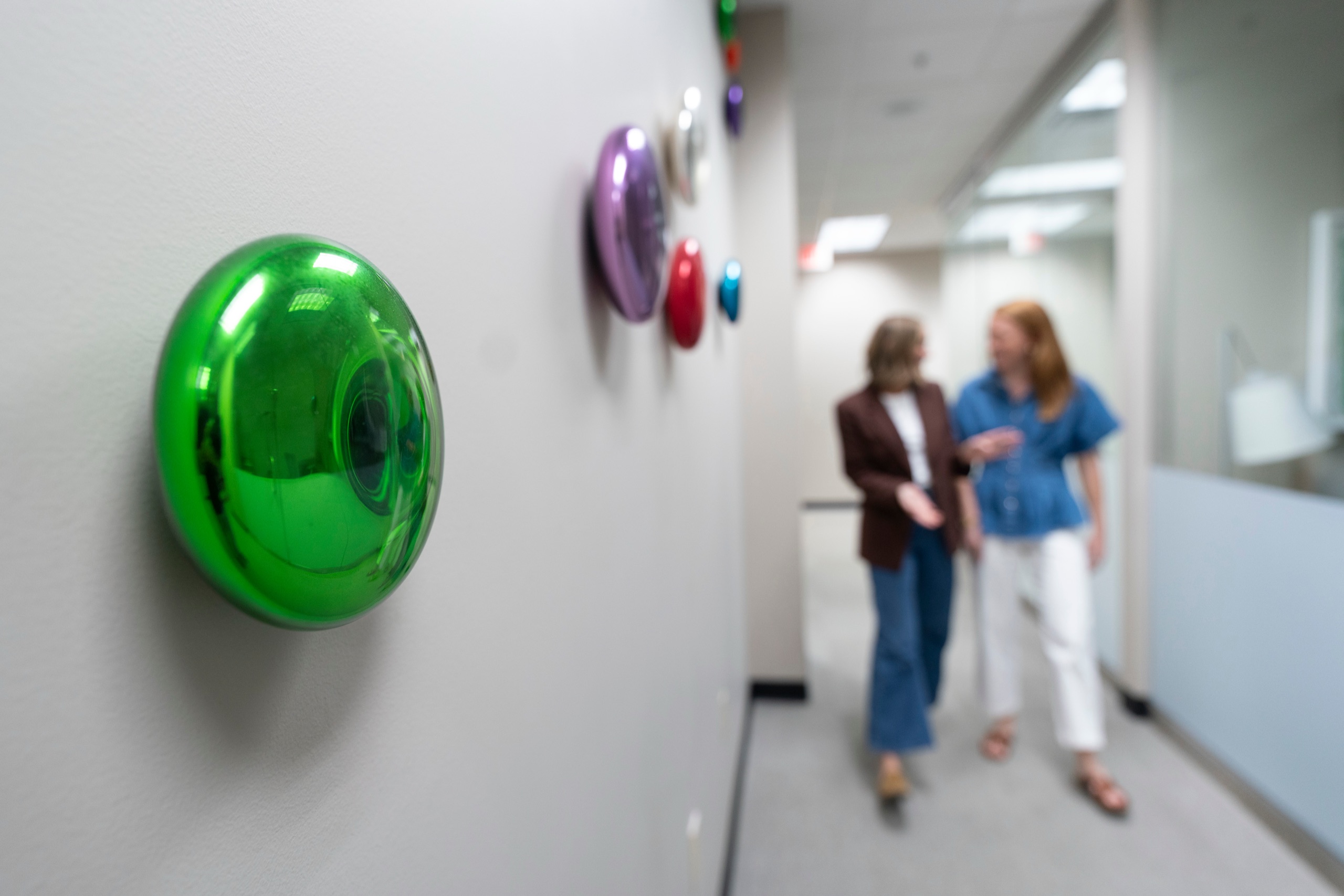Two colleagues talking in an office hallway with colorful disc wall art