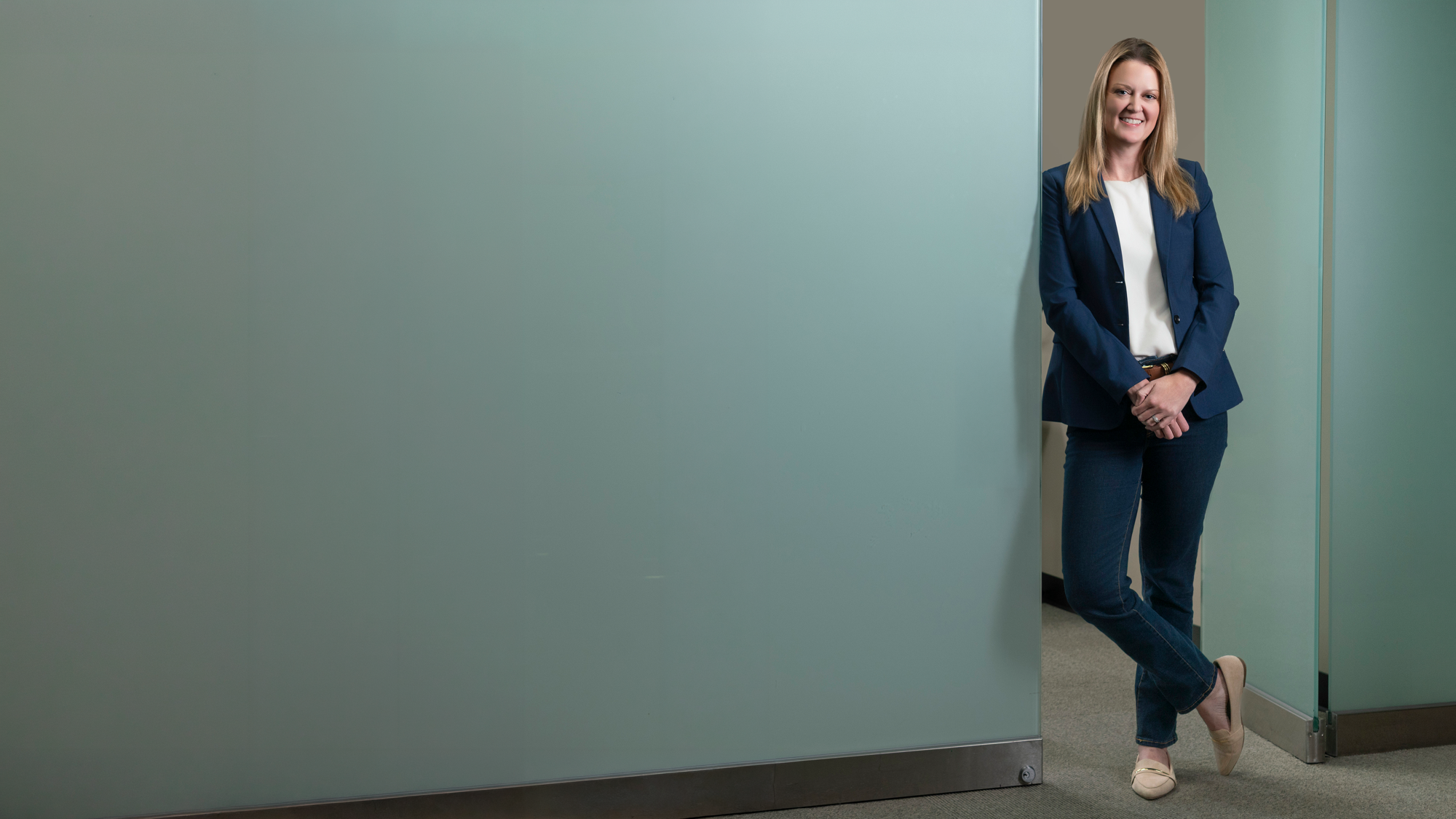 Smiling professional in a navy blazer beside a frosted-glass office wall